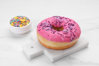 Photo of Sweet glazed donut decorated with sprinkles on white marble table. Tasty confectionery