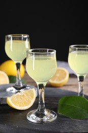 Photo of Tasty limoncello liqueur, lemon and green leaf on table, closeup