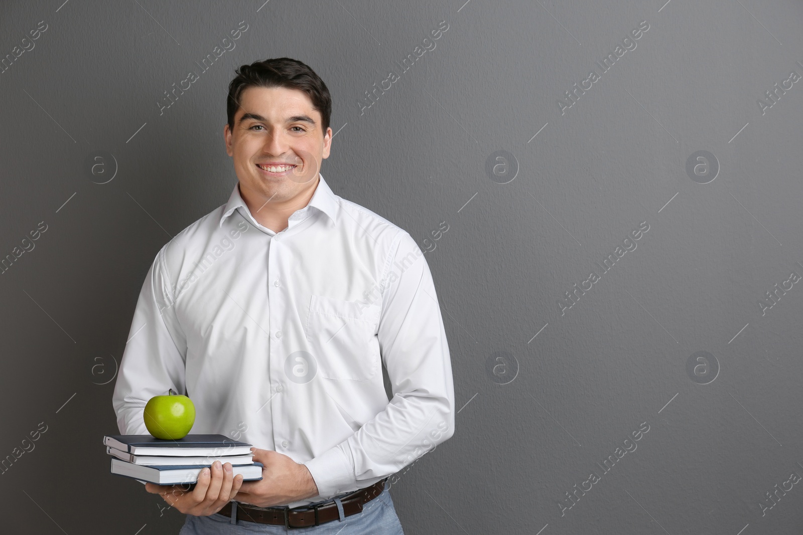 Photo of Portrait of male teacher with notebooks and apple on grey background