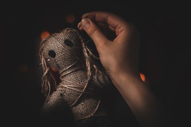 Image of Woman stabbing voodoo doll with pin on dark background, closeup. Curse ceremony