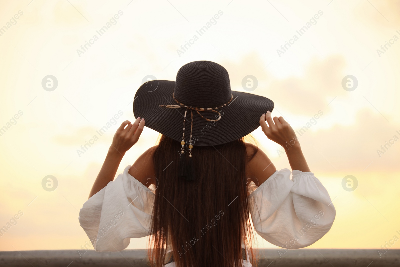 Photo of Young woman in hat at sunset, back view