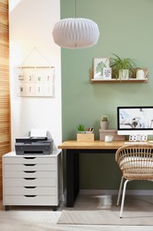 Photo of Stylish workplace with computer, printer and houseplant near olive wall at home