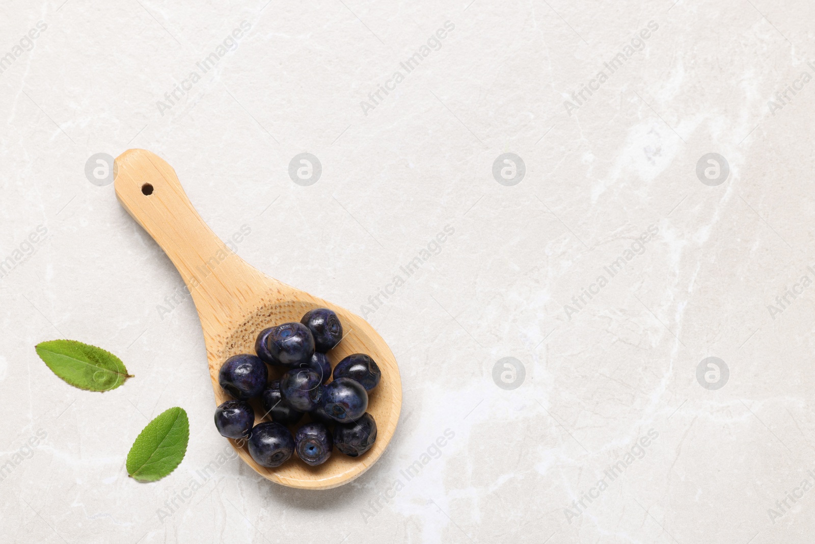 Photo of Spoon with tasty fresh bilberries and green leaves on white table, flat lay. Space for text