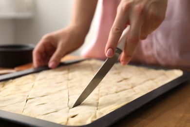 Photo of Making delicious baklava. Woman cutting dough in baking pan at wooden table, closeup