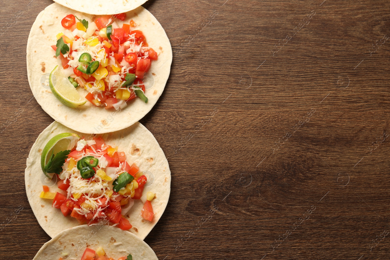 Photo of Delicious tacos with vegetables and lime on wooden table, top view. Space for text