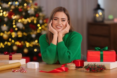 Photo of Beautiful young woman, Christmas gifts and decor at table in room