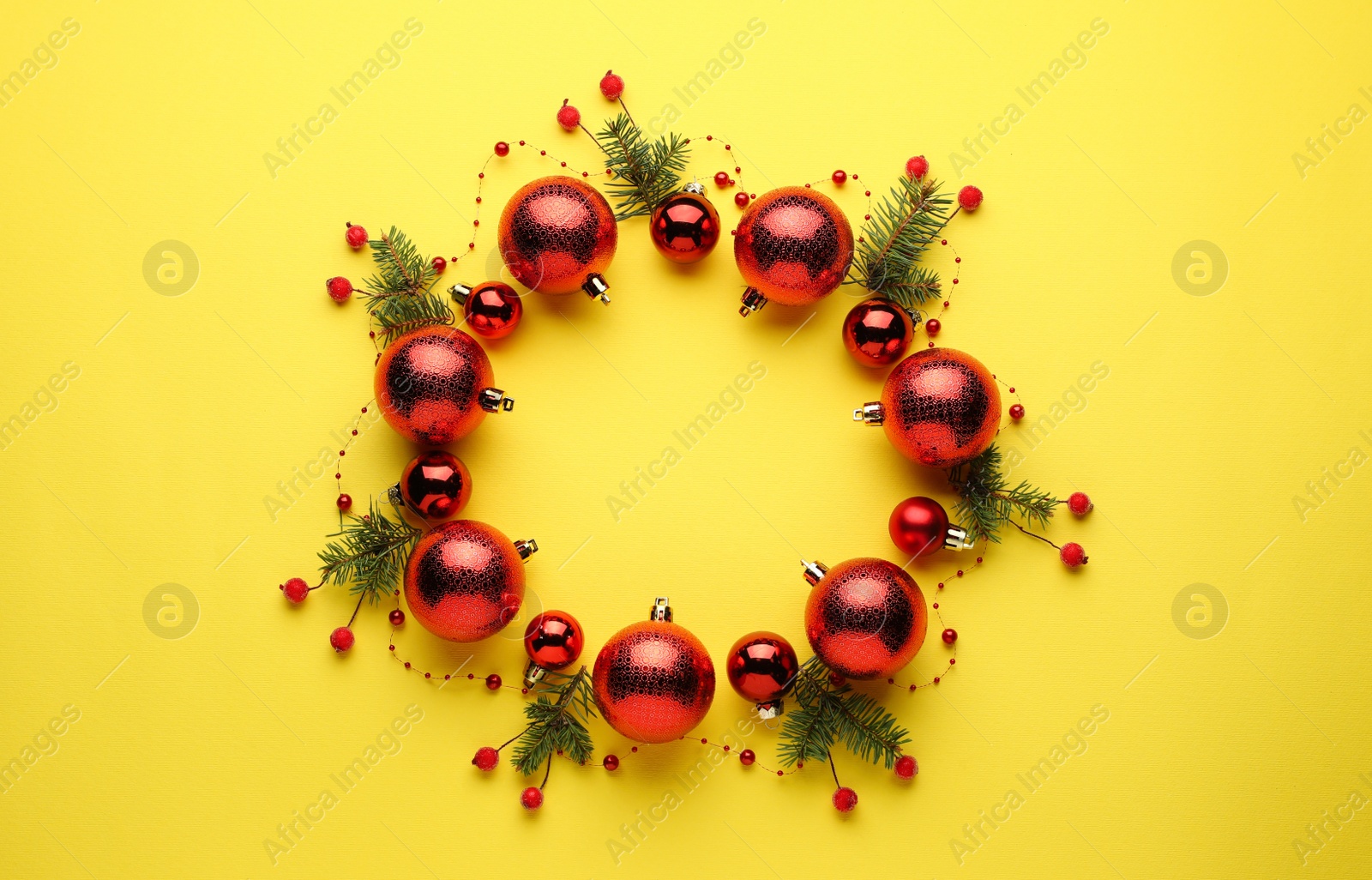 Photo of Bright festive wreath made of Christmas balls and fir branches on yellow background, top view. Space for text