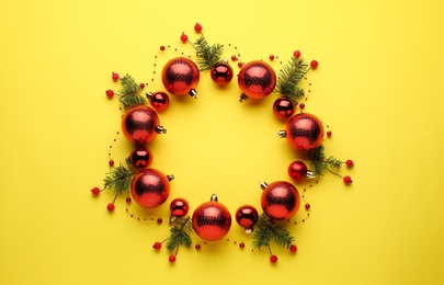 Photo of Bright festive wreath made of Christmas balls and fir branches on yellow background, top view. Space for text