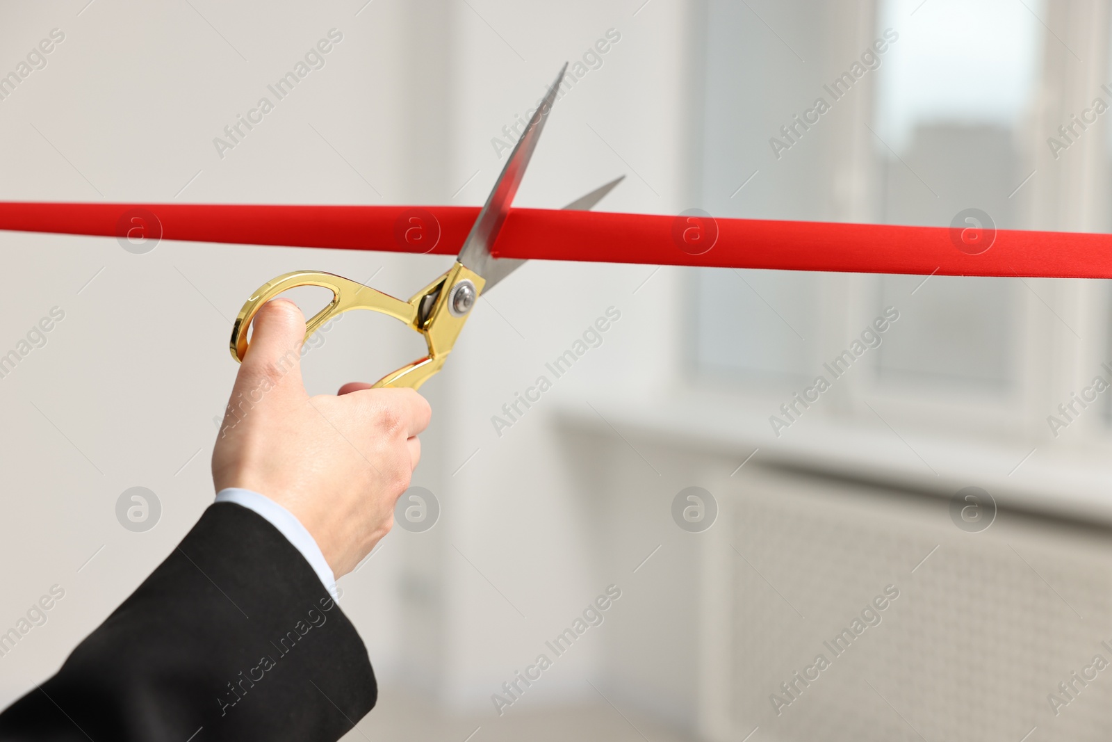 Photo of Woman cutting red ribbon with scissors indoors, closeup