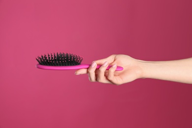 Woman holding hair brush against crimson background, closeup