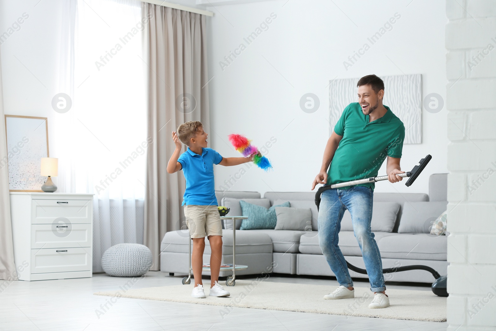 Photo of Dad and son having fun while cleaning living room together