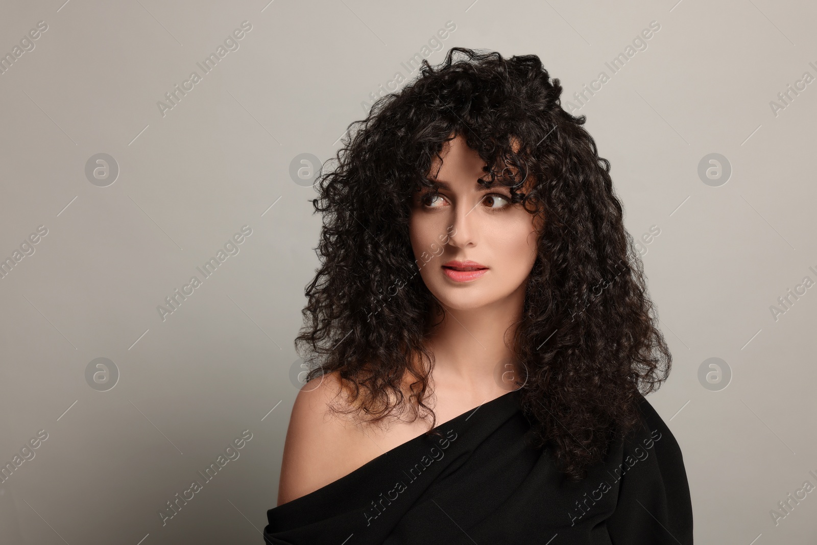 Photo of Beautiful young woman with long curly hair on light grey background. Space for text