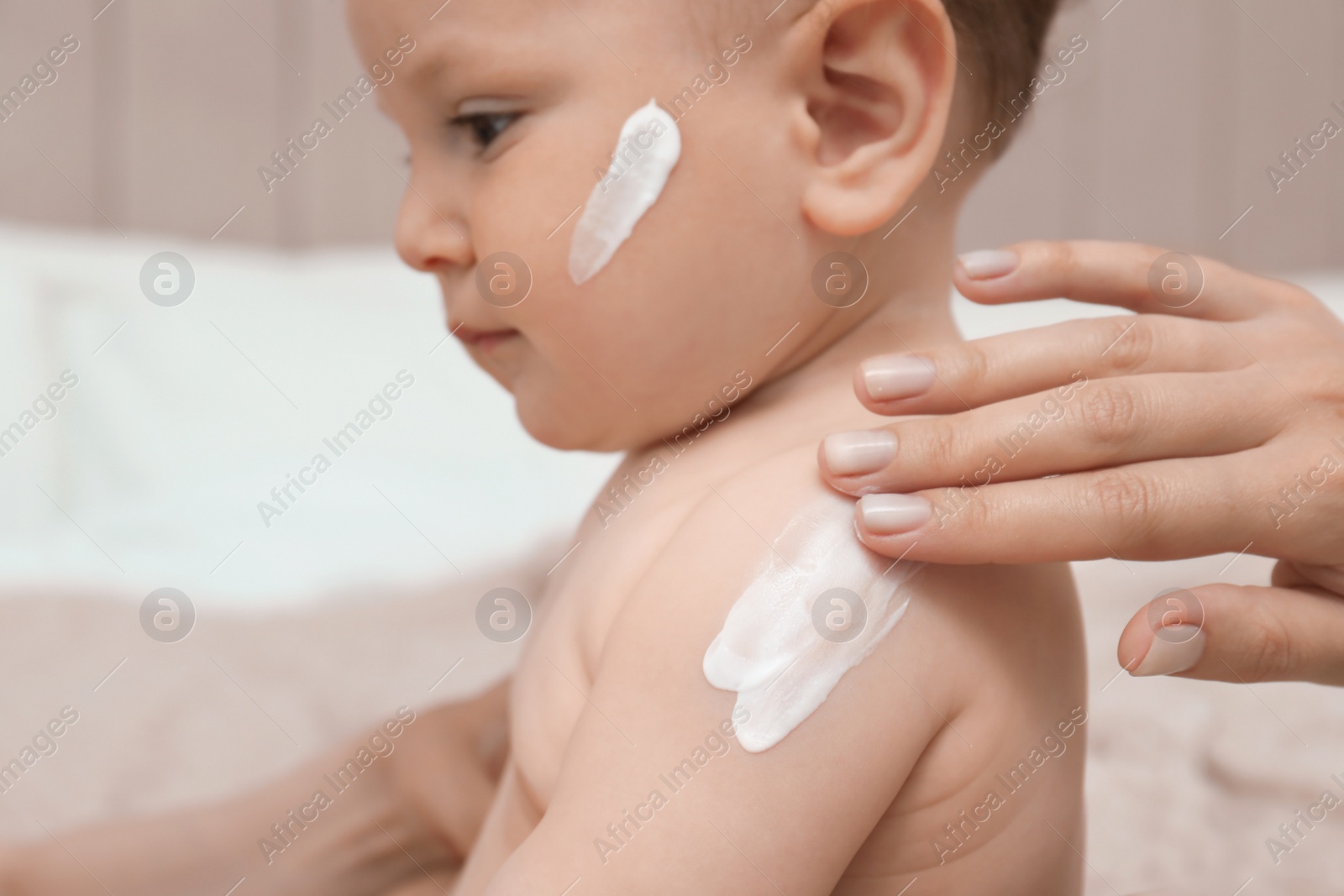 Photo of Mother applying body cream on her baby indoors, closeup