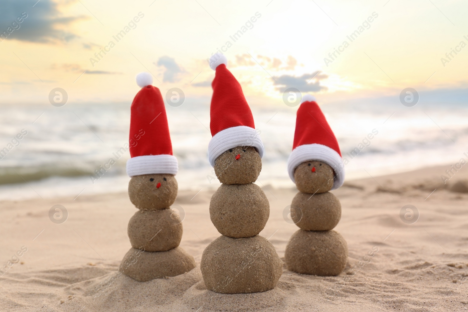 Photo of Snowmen made of sand with Santa hats on beach near sea. Christmas vacation