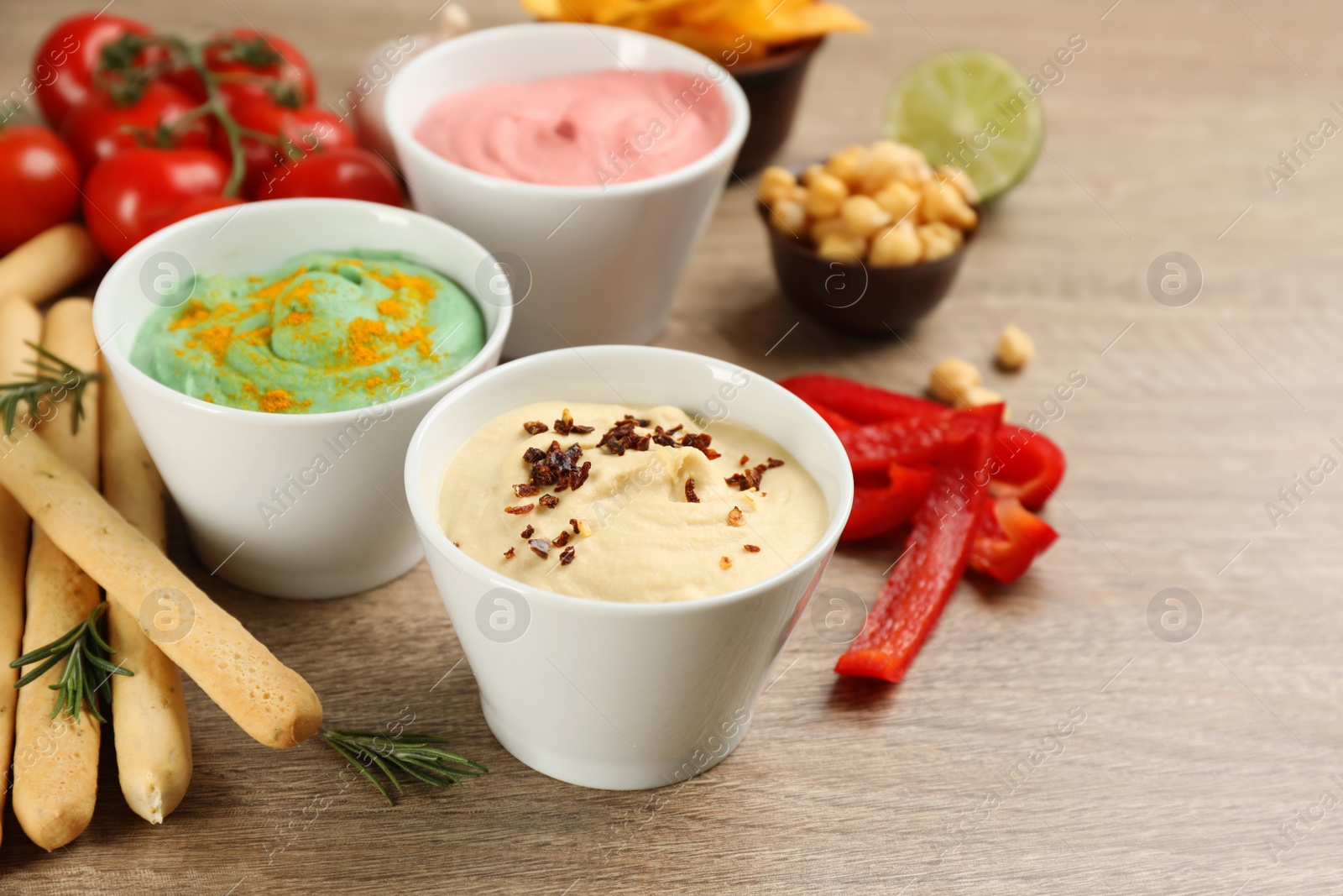 Photo of Different kinds of tasty hummus served with bread sticks on wooden table