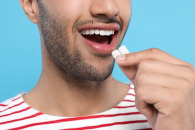 Photo of Man putting bubble gums into mouth on light blue background, closeup