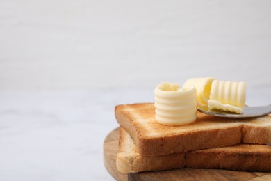 Photo of Tasty butter curls, knife and toasts on white table, closeup. Space for text