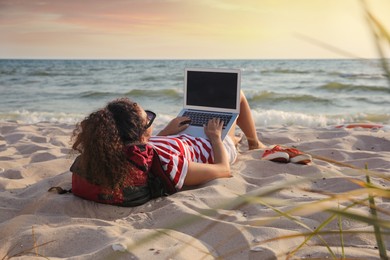 Photo of African American woman working on laptop at beach