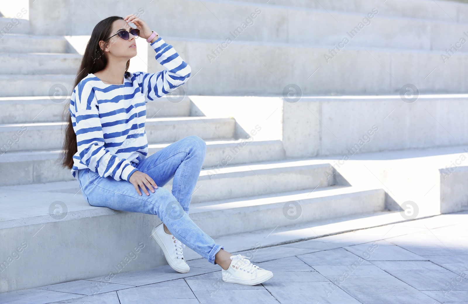 Photo of Young hipster woman in stylish jeans sitting on stairs outdoors