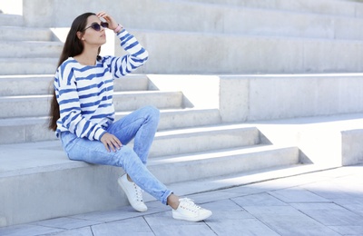 Photo of Young hipster woman in stylish jeans sitting on stairs outdoors