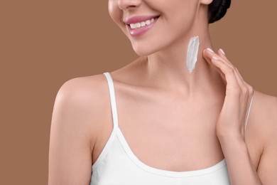 Photo of Woman with smear of body cream on her neck against light brown background, closeup
