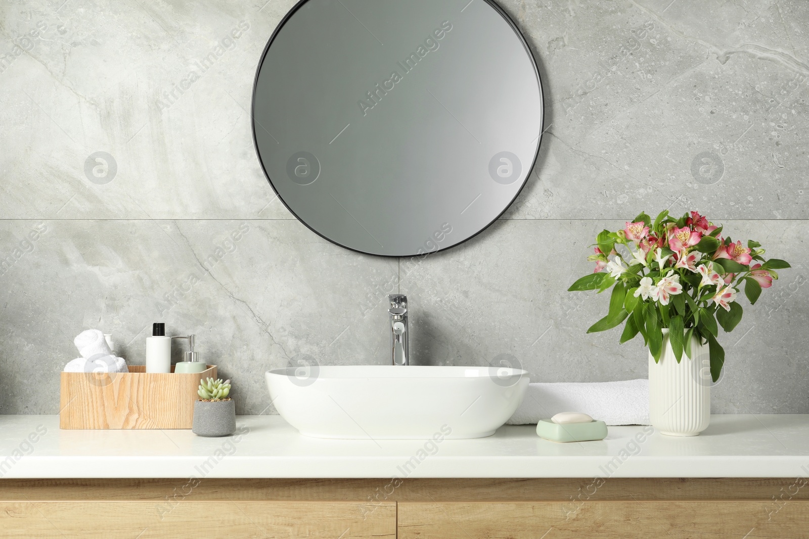 Photo of Vase with beautiful Alstroemeria flowers and toiletries near sink in bathroom