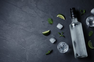 Photo of Bottle of vodka, shot glasses, lime, mint and ice on black table, flat lay. Space for text