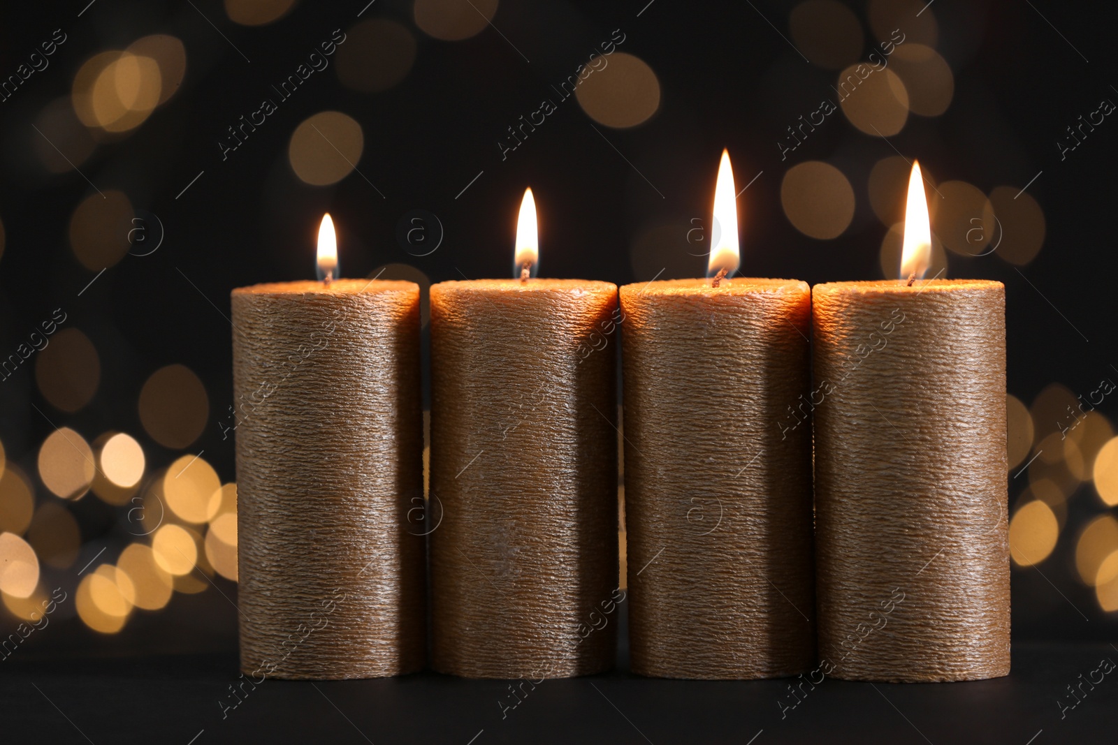 Photo of Burning gold candles against blurred lights in darkness