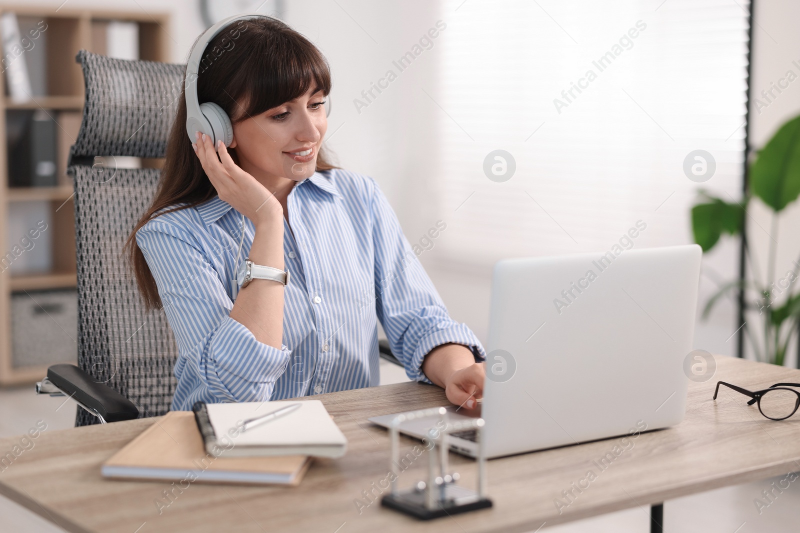 Photo of Woman in headphones watching webinar at wooden table in office