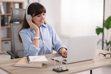 Photo of Woman in headphones watching webinar at wooden table in office