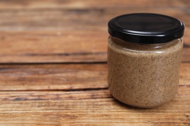 Tasty nut paste in jar on wooden table, closeup. Space for text