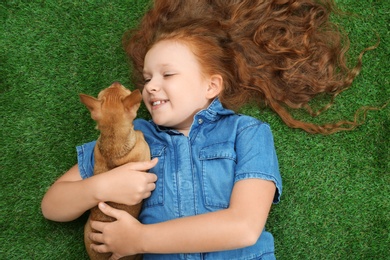 Photo of Little girl with her Chihuahua dog lying on grass, top view. Childhood pet