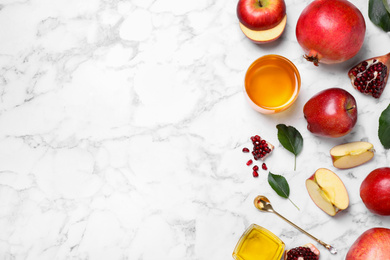 Honey, apples and pomegranates on white marble table, flat lay with space for text. Rosh Hashanah holiday