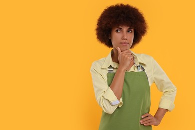 Photo of Thoughtful young woman in apron on orange background. Space for text