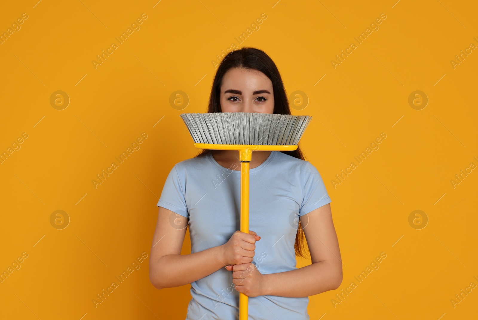 Photo of Beautiful young woman with broom on yellow background