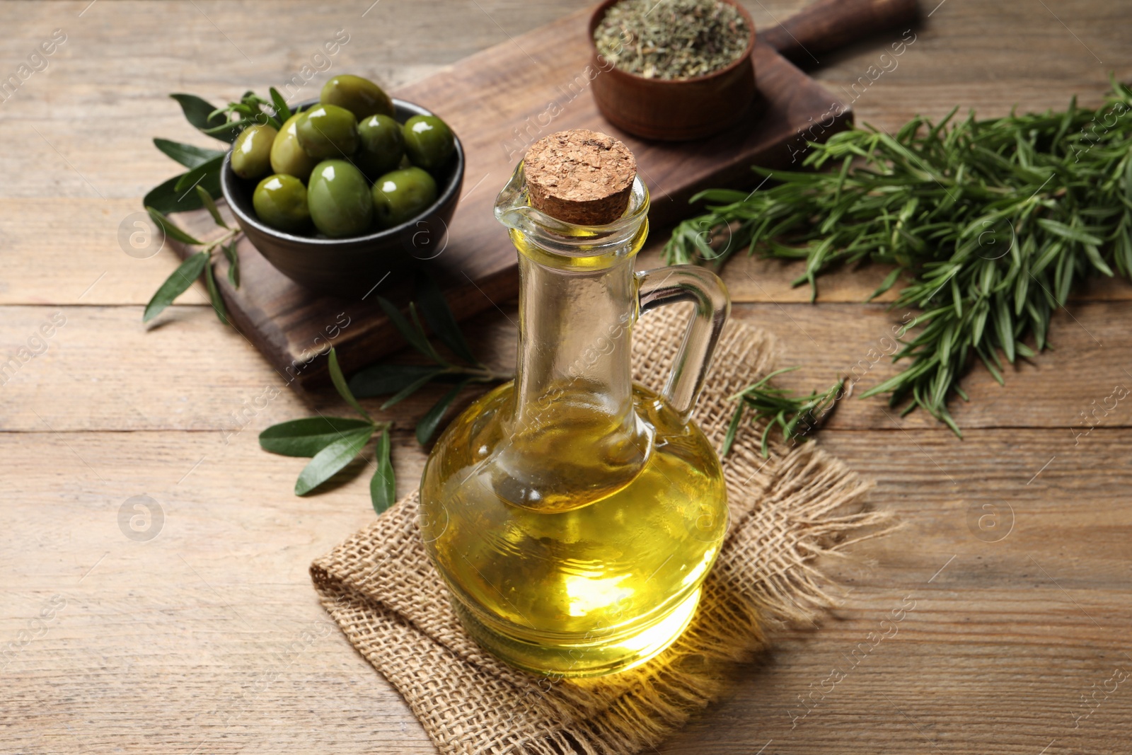 Photo of Glass jug of oil, ripe olives and green leaves on wooden table