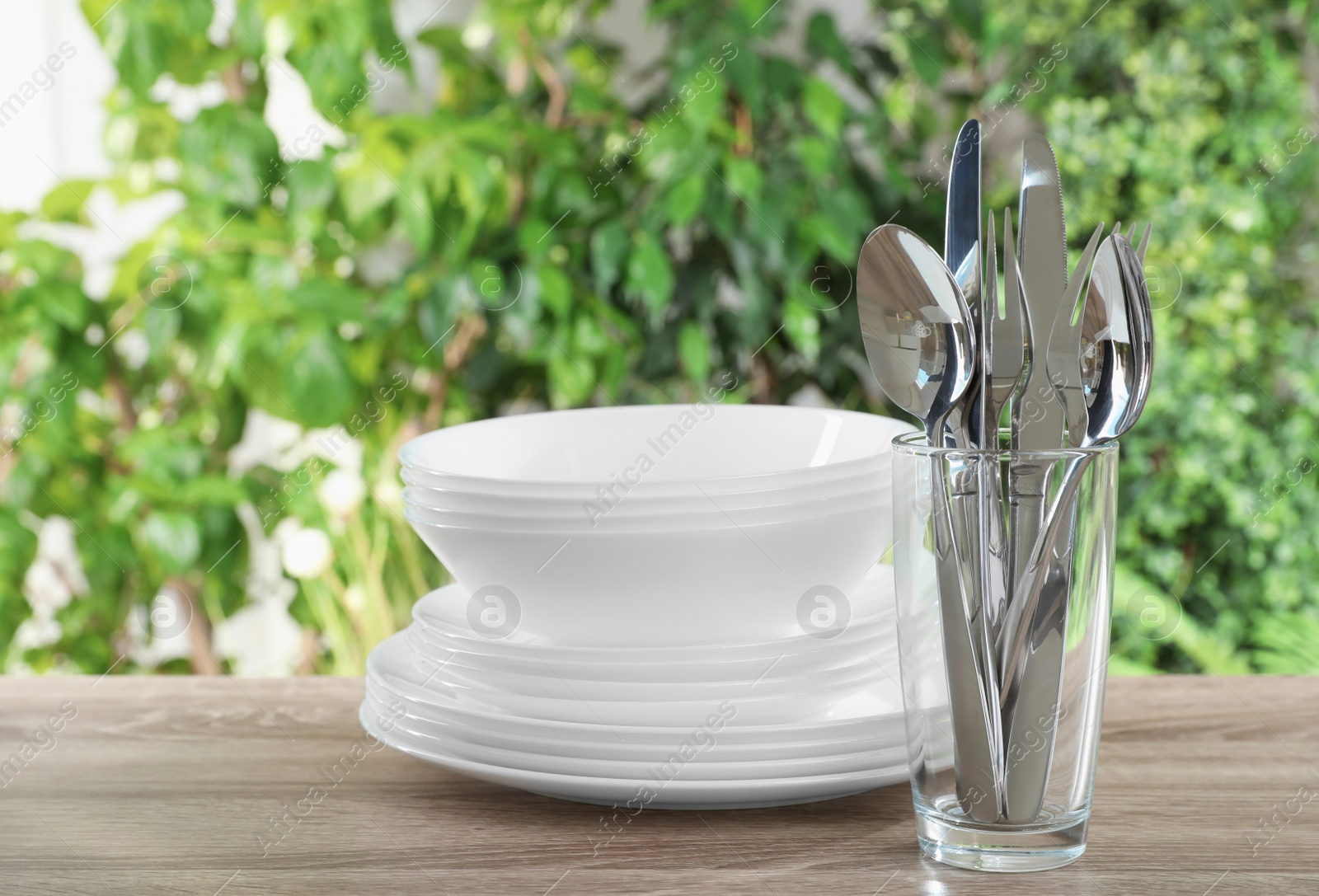 Photo of Clean dishes and glass with shiny cutlery on wooden table against blurred background