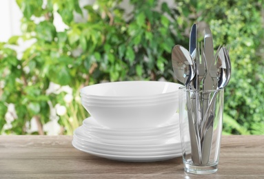 Clean dishes and glass with shiny cutlery on wooden table against blurred background