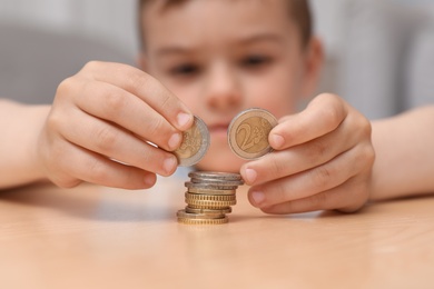 Photo of Cute little boy stacking coins at home, focus on hands