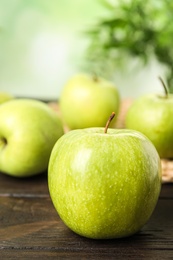 Photo of Fresh ripe green apple on dark wooden table against blurred background, closeup view. Space for text