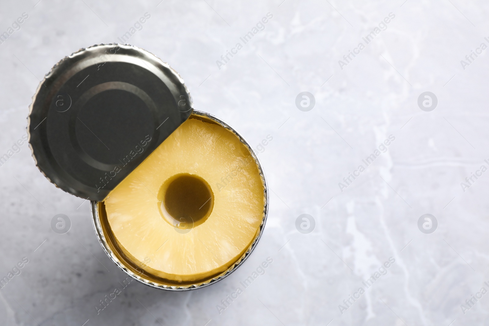 Photo of Open tin with canned pineapple on light grey marble table, top view. Space for text