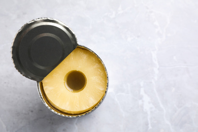 Photo of Open tin with canned pineapple on light grey marble table, top view. Space for text