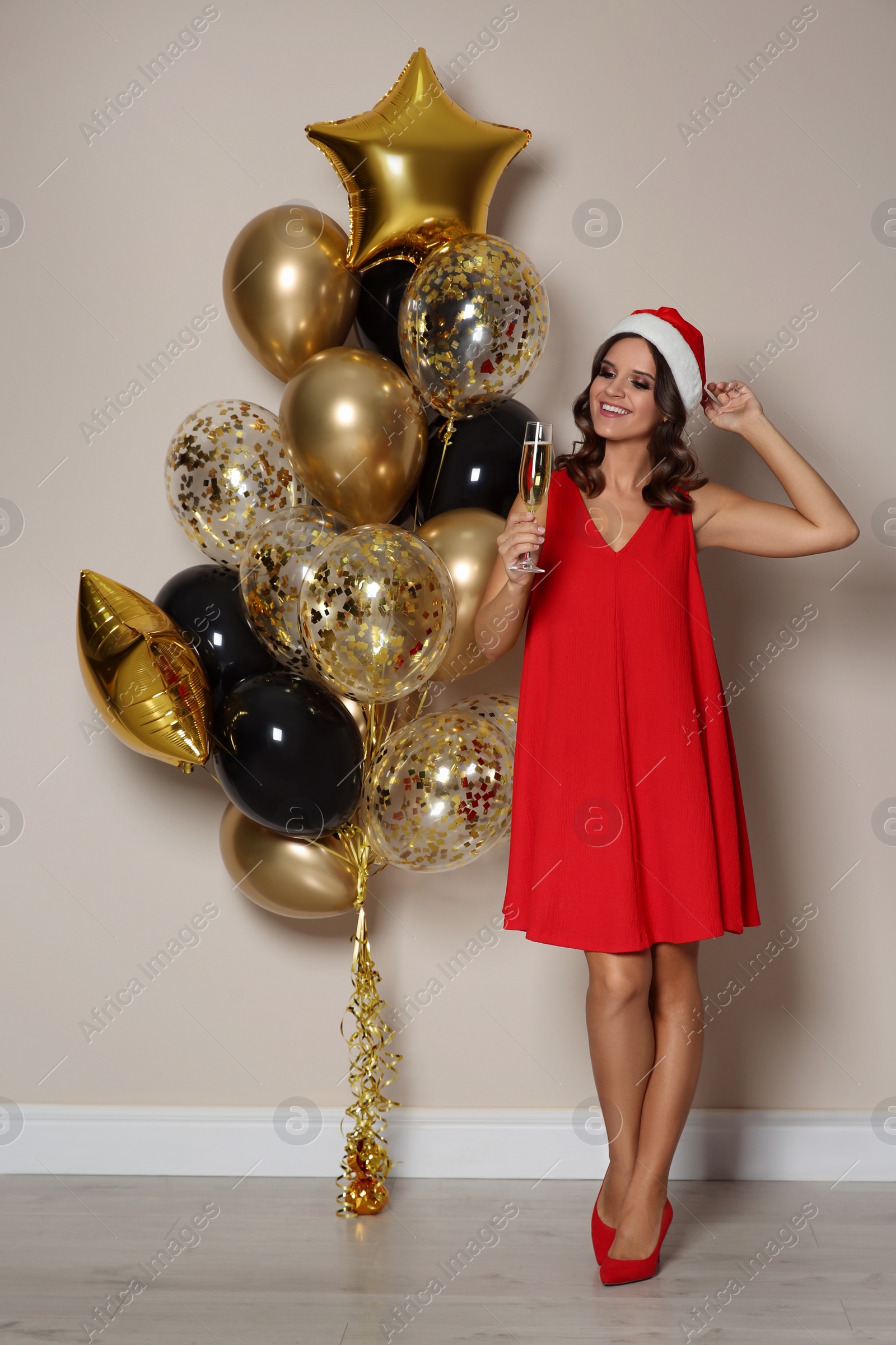 Photo of Happy woman in Santa hat with air balloons near beige wall indoors. Christmas party