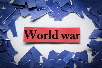 Photo of Words World War and pieces of torn blue paper on white background, flat lay