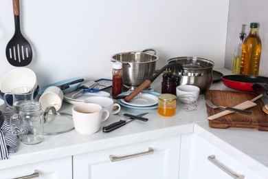 Photo of Many dirty utensils, cookware and dishware on countertop in messy kitchen