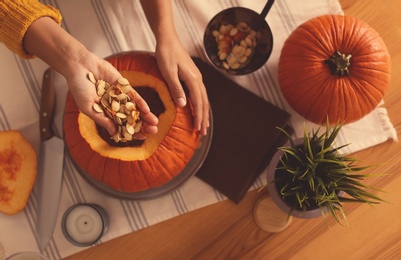 Photo of Woman making pumpkin jack o'lantern at table, top view. Halloween celebration