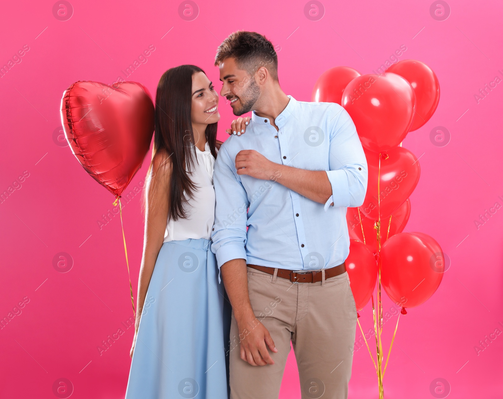 Photo of Young couple and air balloons on pink background. Celebration of Saint Valentine's Day