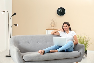 Photo of Beautiful woman with laptop sitting on sofa at home