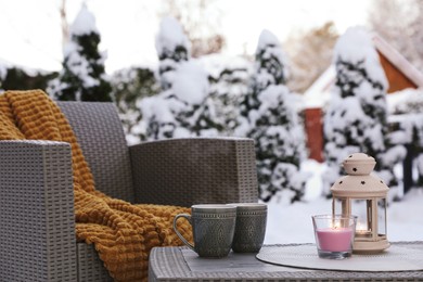 Burning candle, lantern and cups with hot drink on coffee table outdoors. Cosy winter