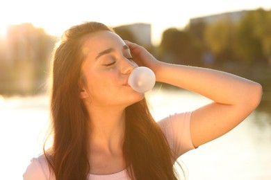 Photo of Beautiful young woman blowing bubble gum outdoors